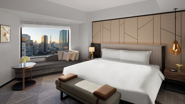 Une chambre d’hôtel moderne dotée d’un grand lit, d’un coin salon avec vue sur la ville et d’une vue panoramique sur le paysage urbain, visible à travers la fenêtre.