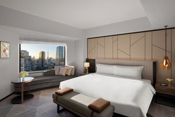 A modern hotel room with a large bed, a seating area with a view of the city, and a cityscape visible through the window.