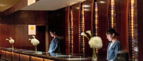 A reception desk with a marble counter, wooden paneling, and two vases with white flowers.