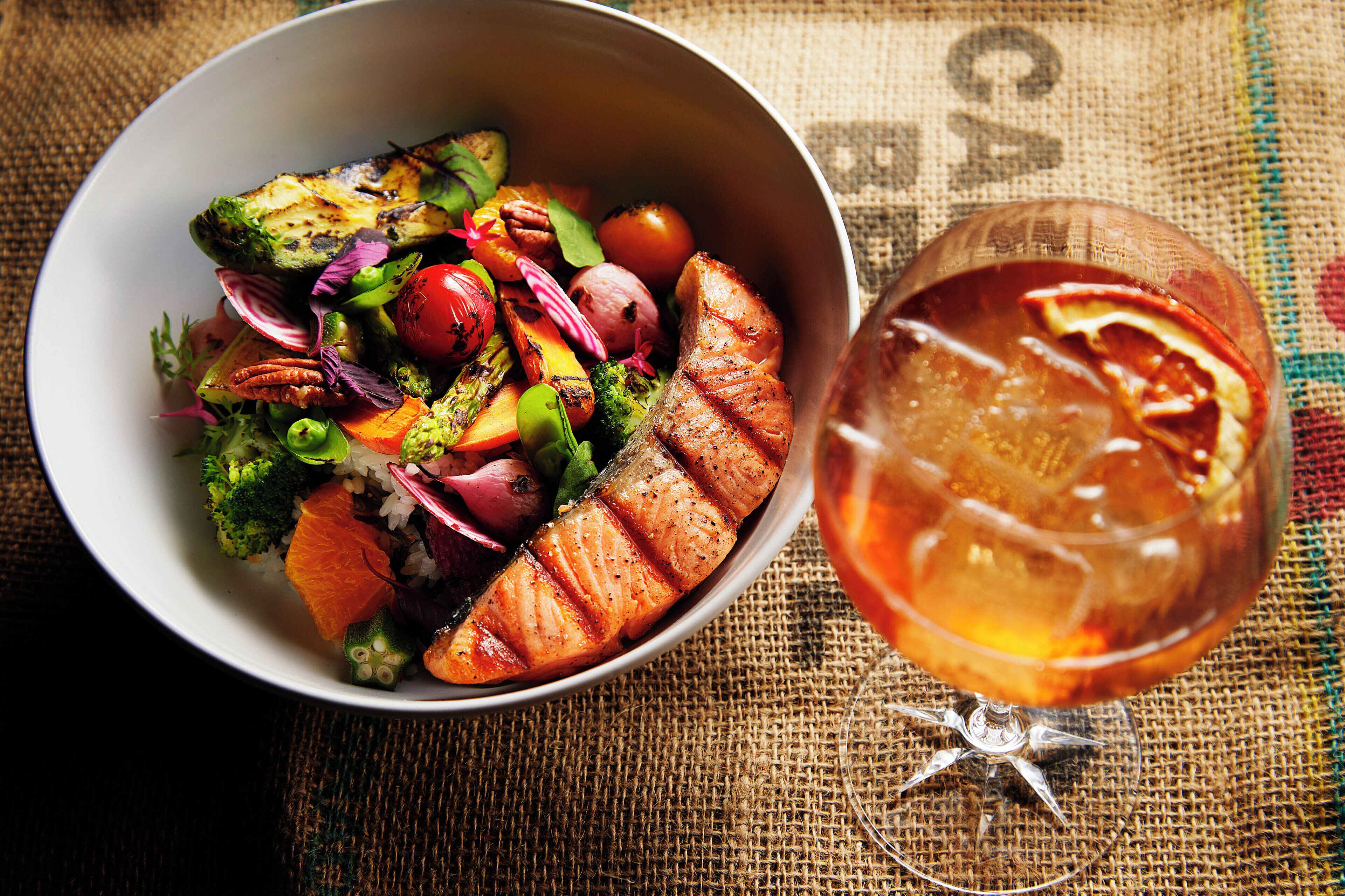 A bowl of food with a glass of drink on a textured surface.