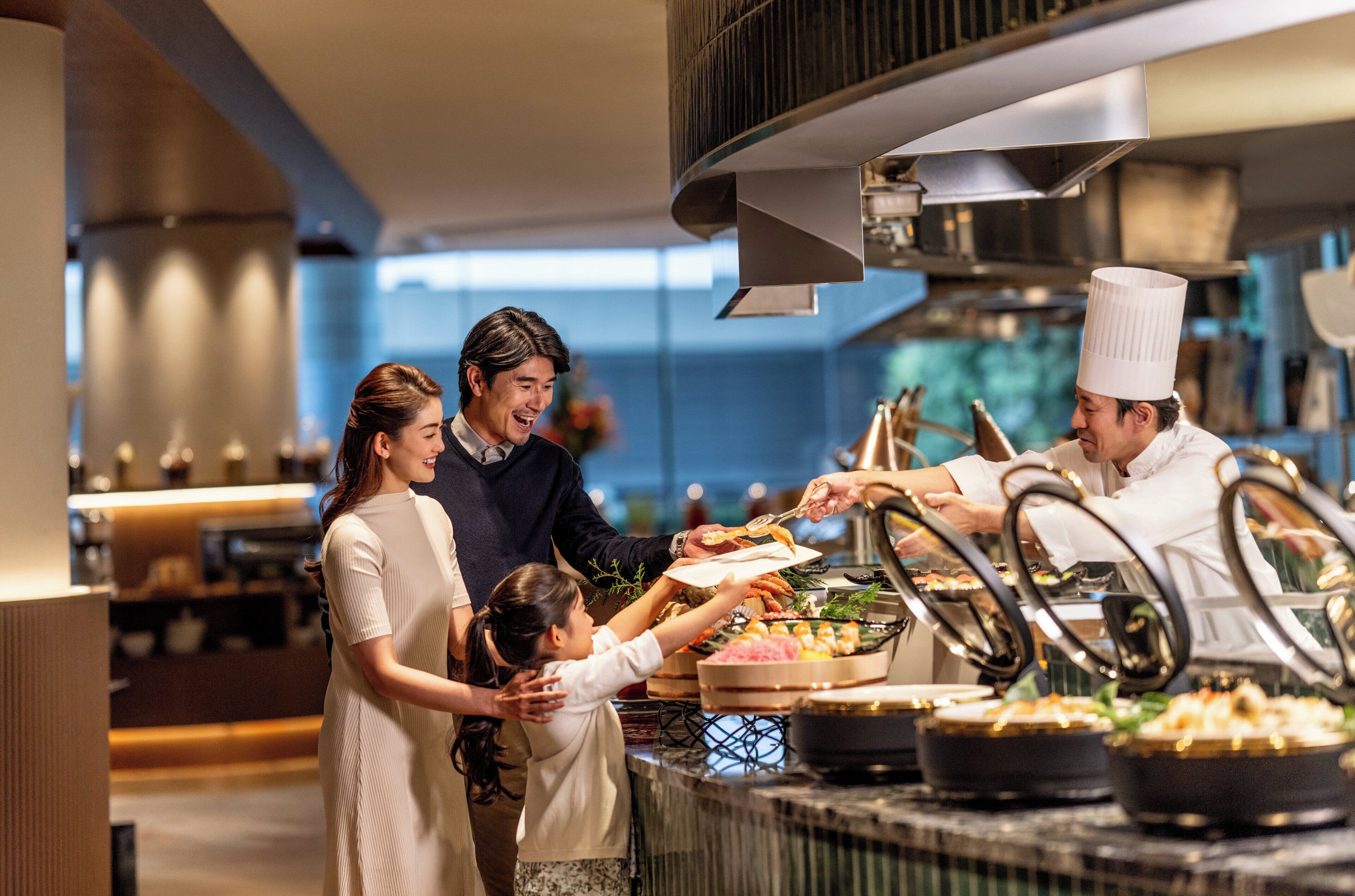A family at a buffet with various dishes and a chef serving food.