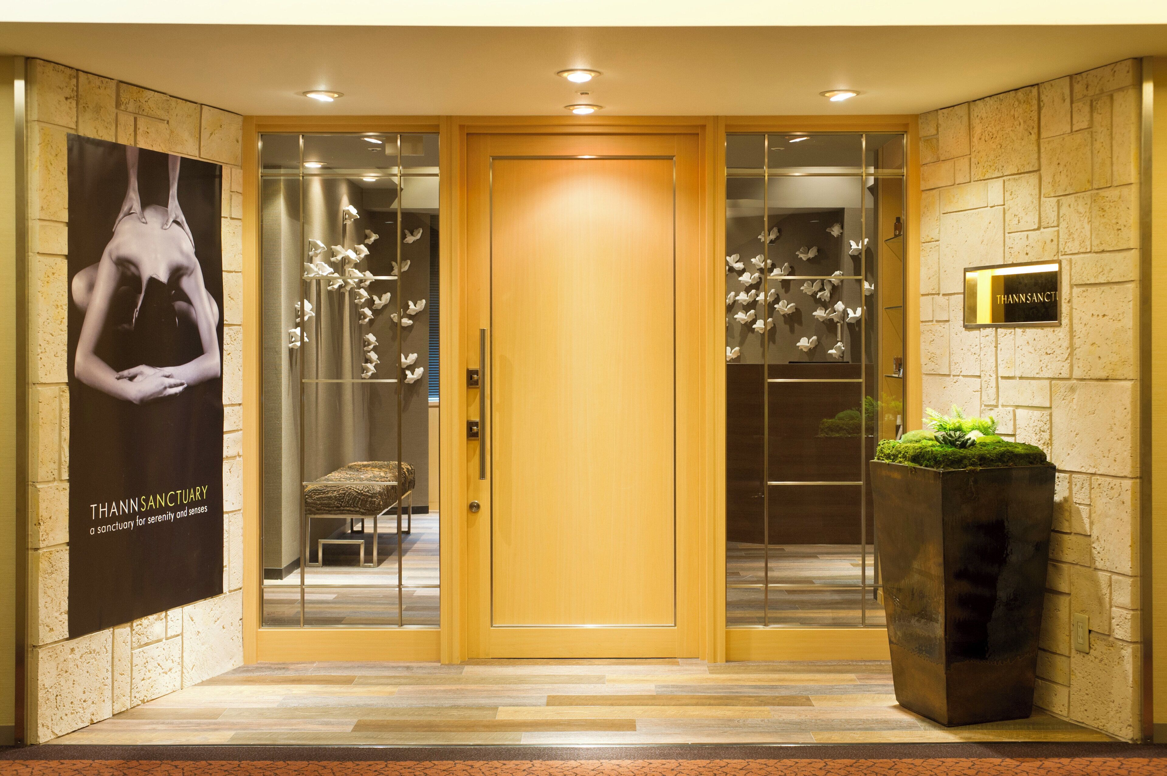 A hotel entrance with a wooden door, a glass door, a bench, a potted plant, and a wall-mounted sign.