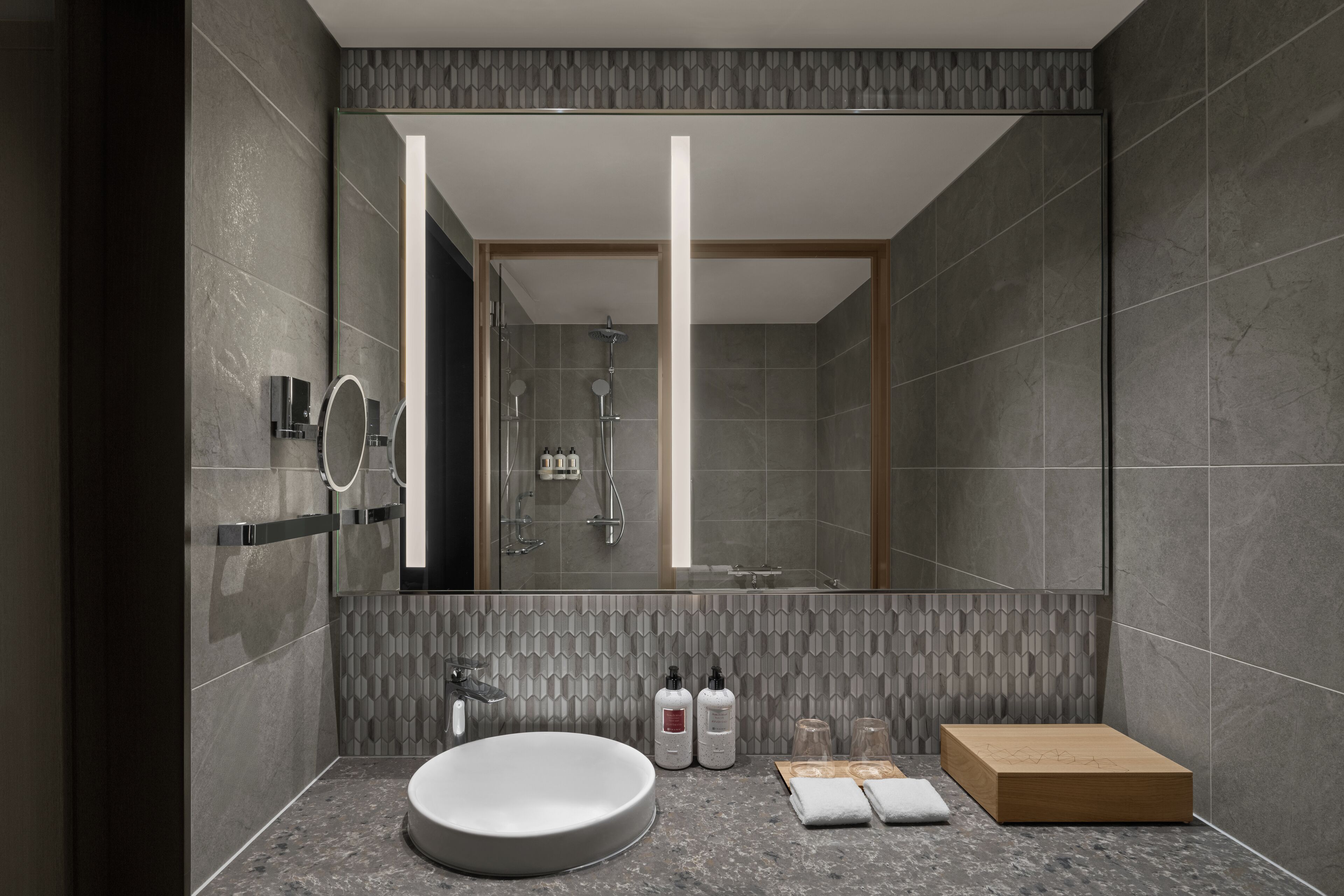 A modern bathroom with a large mirror, a round sink, and a shower area.
