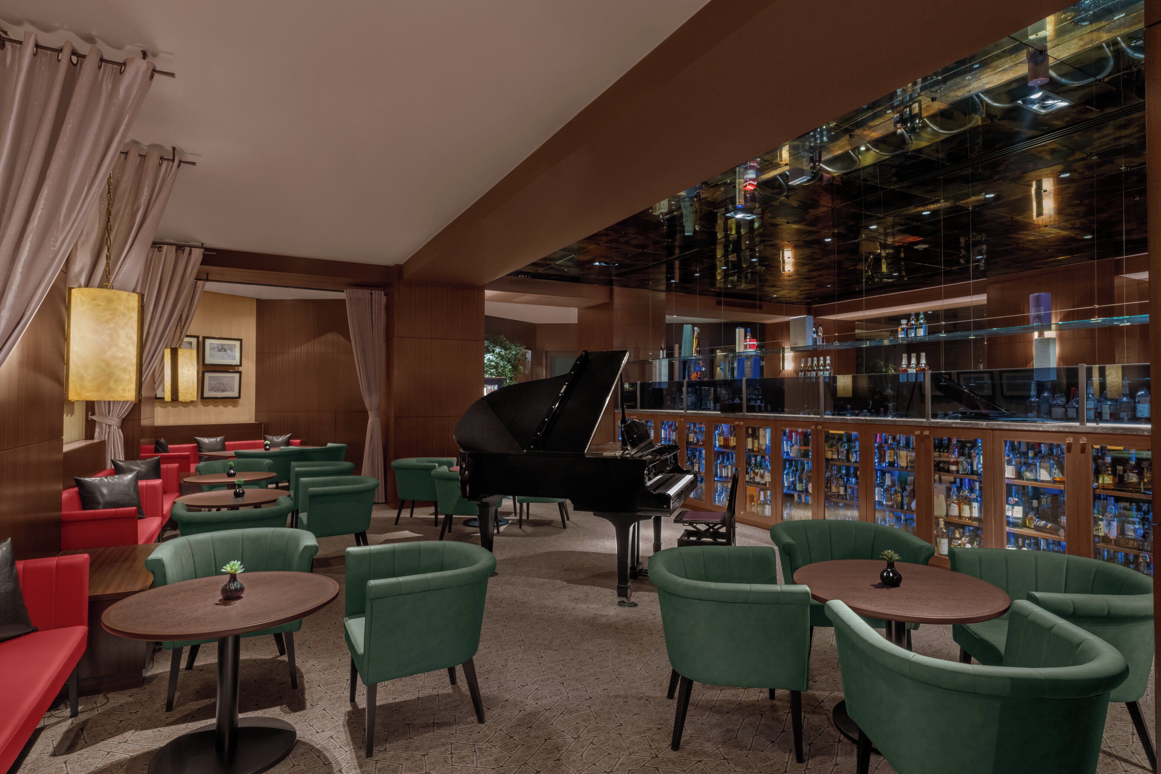 Zona de bar con un piano de cola, sillas verdes y una estantería para vinos.