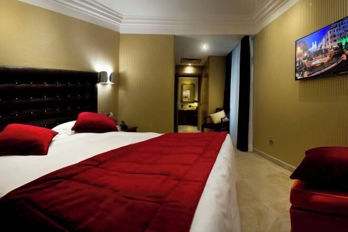 Une chambre d’hôtel avec un grand lit, un plaid rouge, un téléviseur fixé au mur et une chaise rouge.