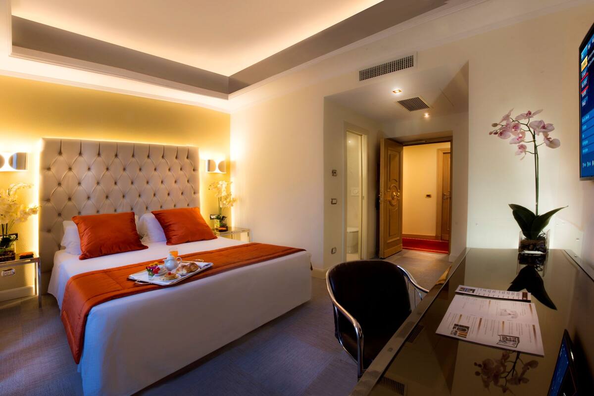 Camera d'albergo con un letto grande, una scrivania con una sedia e un tavolino con un vaso di fiori.