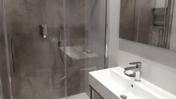 A modern bathroom with a glass-enclosed shower, a white sink, and a large mirror.