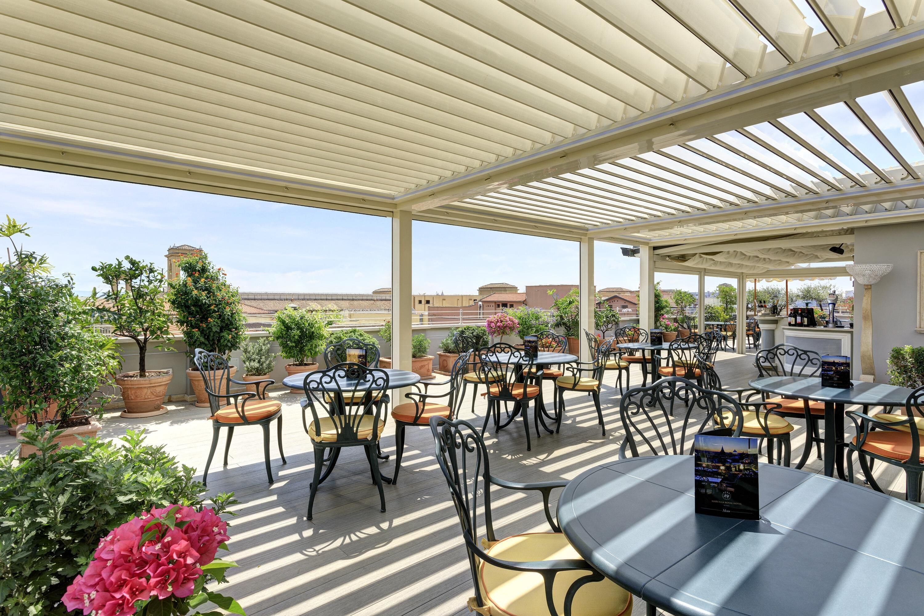 Eine Terrasse im Freien mit Tischen und Stühlen, umgeben von Blumentöpfen und Blumen.
