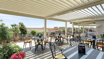Eine Terrasse im Freien mit Tischen und Stühlen, umgeben von Blumentöpfen und Blumen.