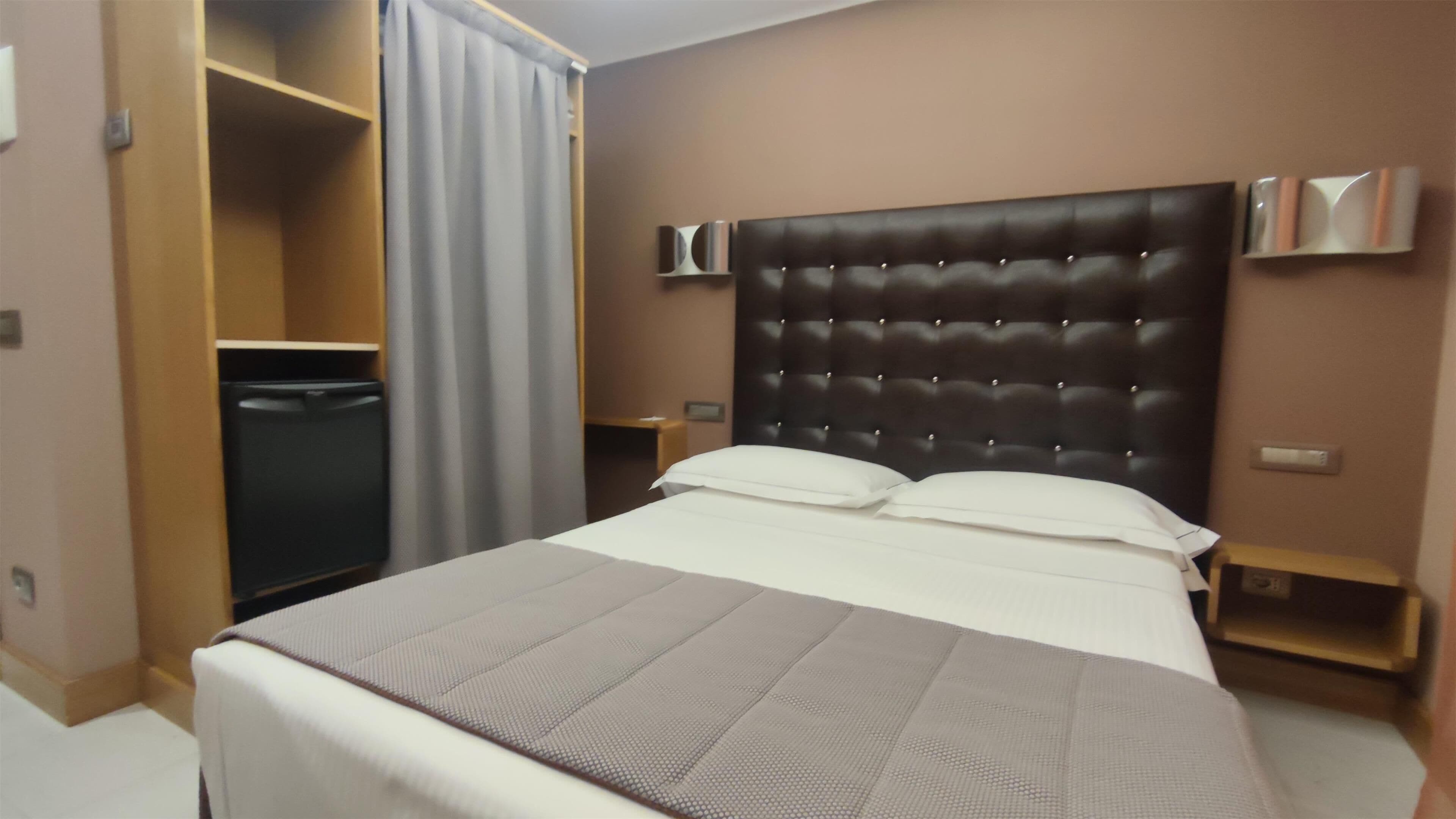 Una habitación de hotel con una cama grande, un armario, una mesita de noche y un tocador.
