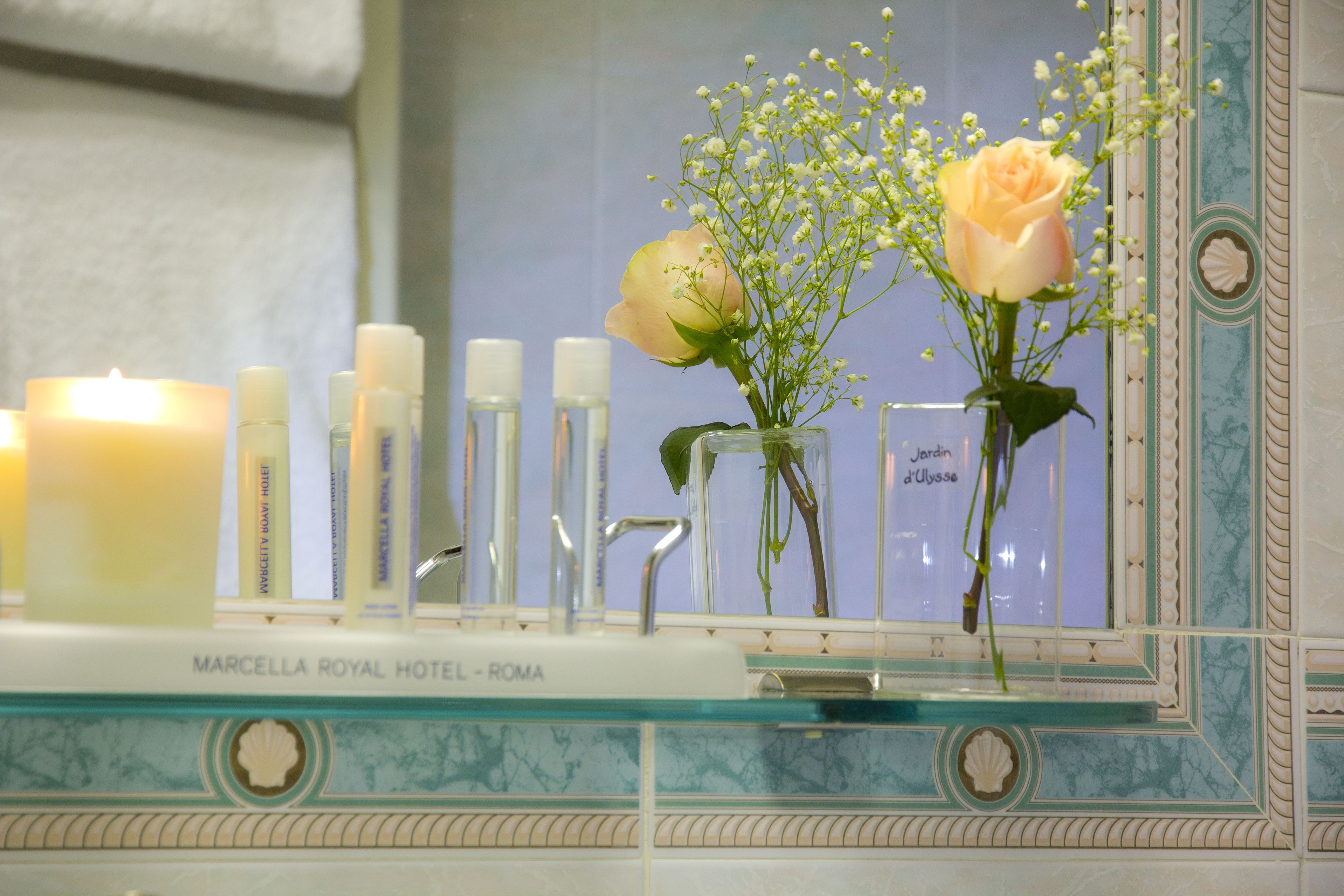 Ein Badezimmer-Waschtisch mit Spiegel, Kerzen, Pflegeprodukten und einer Blumenvase.