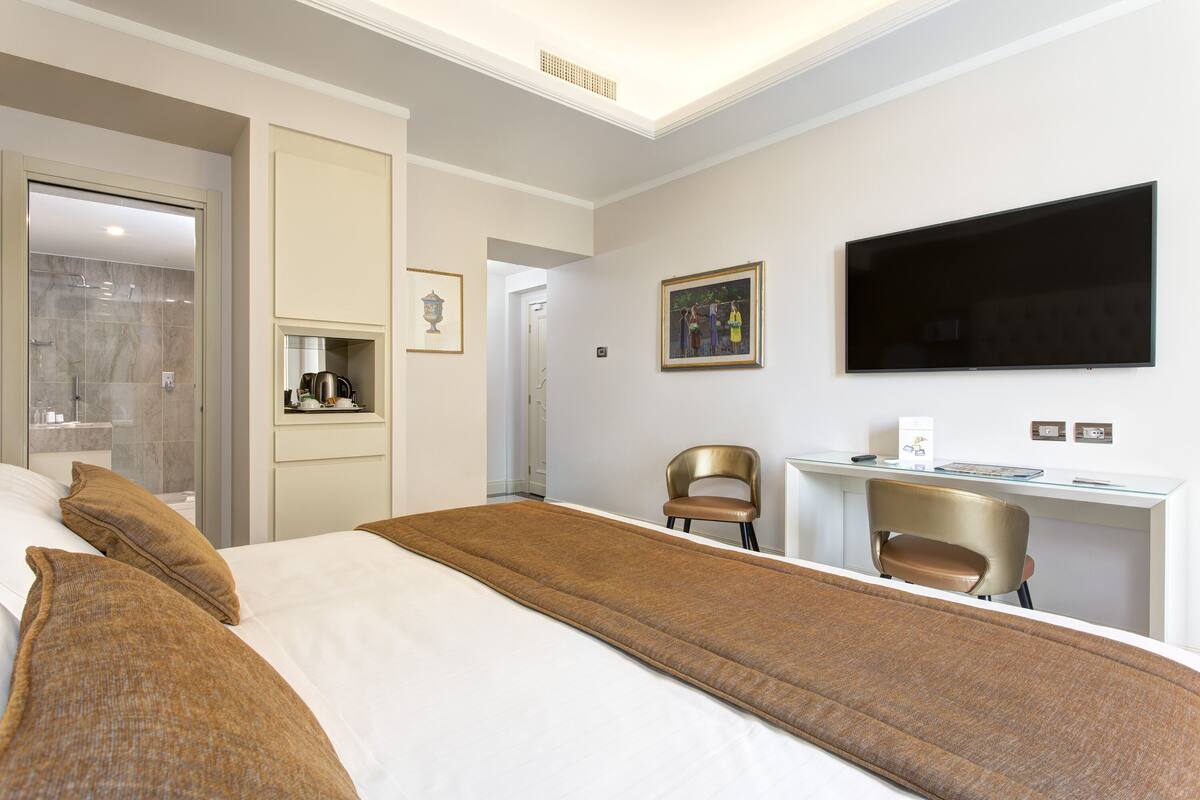 Una camera d'albergo con un letto grande, una scrivania, una sedia, un televisore e uno spazio doccia.