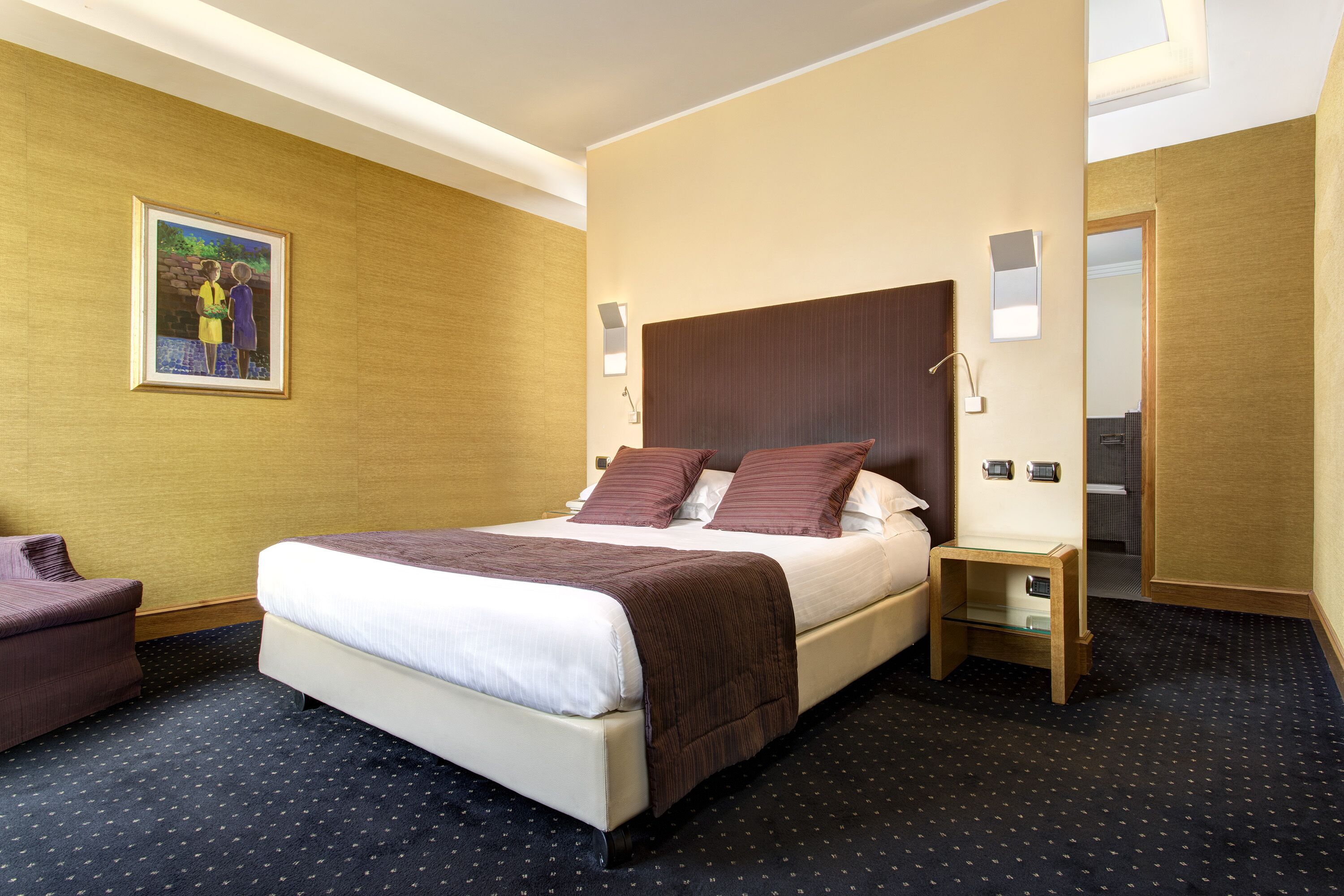 A hotel room with a large bed, a bedside table, a chair, and a painting on the wall.