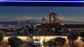 A rooftop terrace with a table set for dining, overlooking a cityscape with historic buildings and a prominent archway.