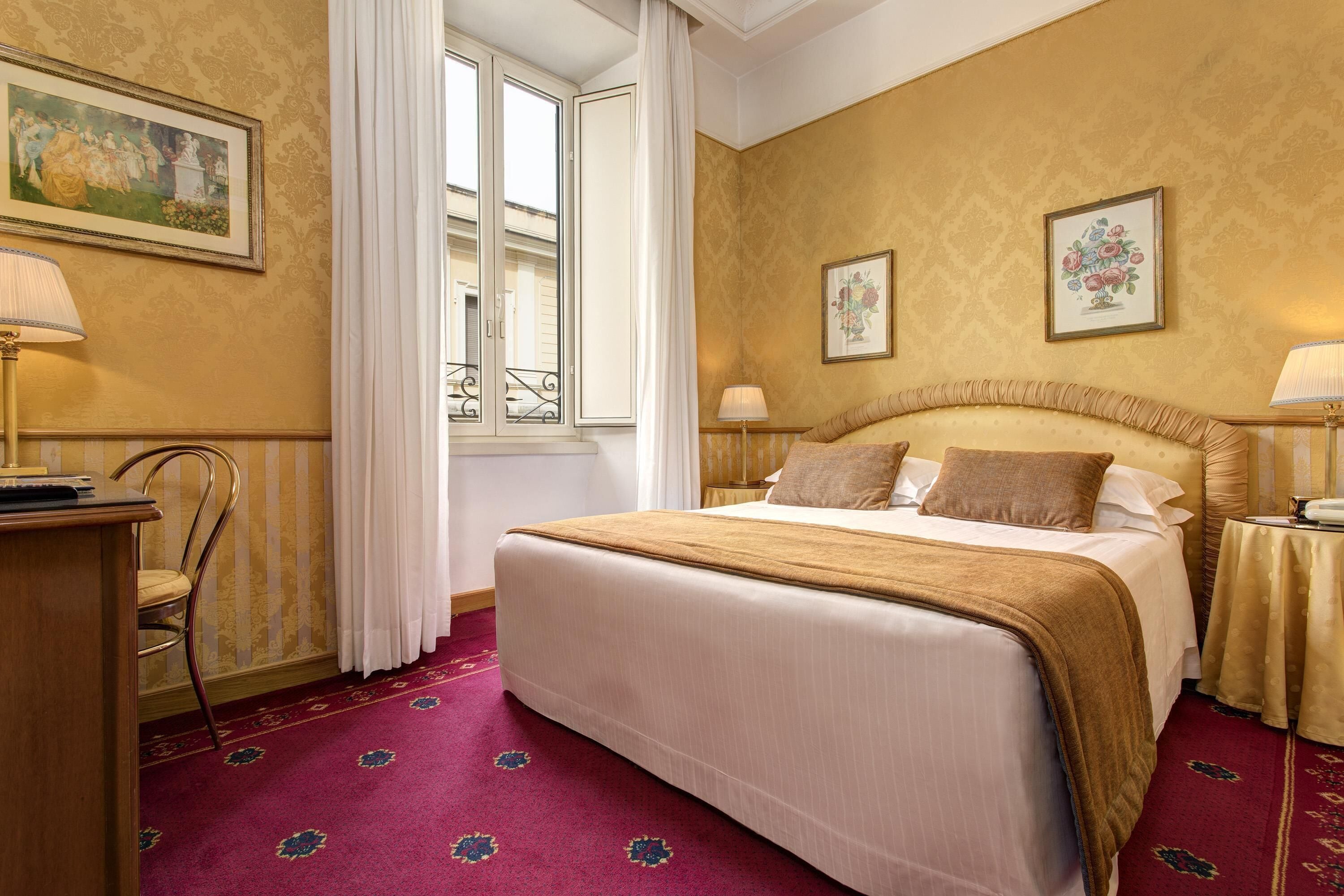 A hotel room with a large bed, two bedside tables with lamps, a chair, and a window with curtains.
