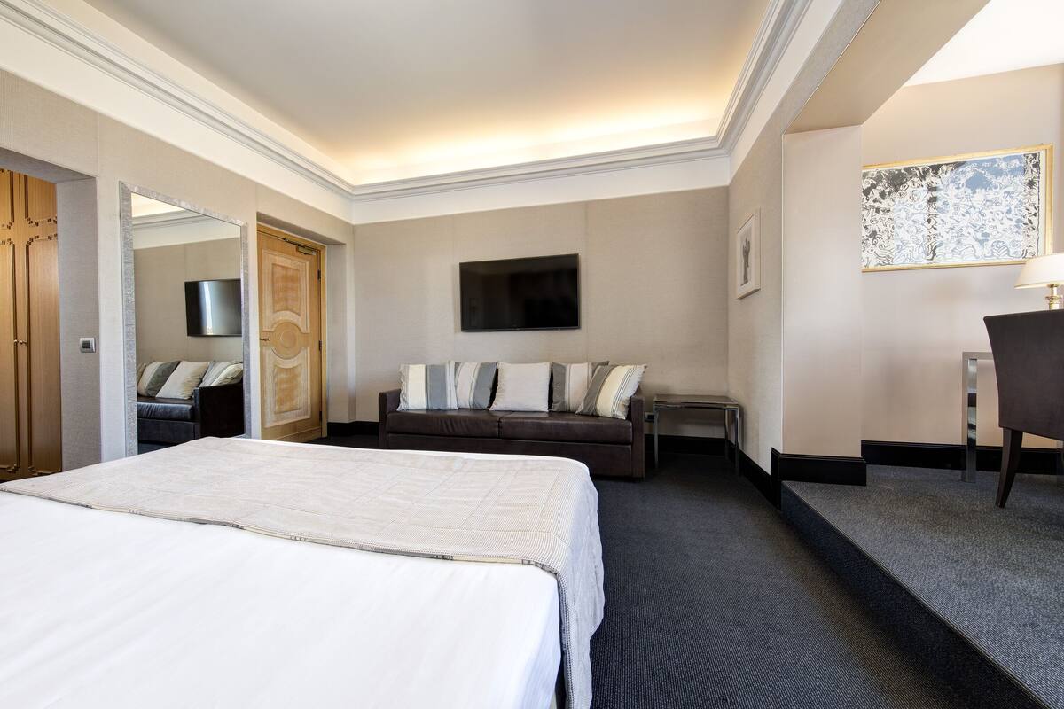 Camera d'albergo con un letto grande, un divano, una televisione appesa al muro e una scrivania con una sedia.