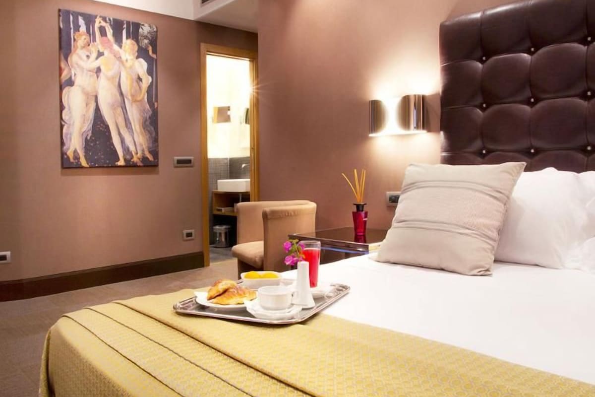 Una habitación de hotel con una cama, una mesa para desayunar, un cuadro en la pared y una silla.