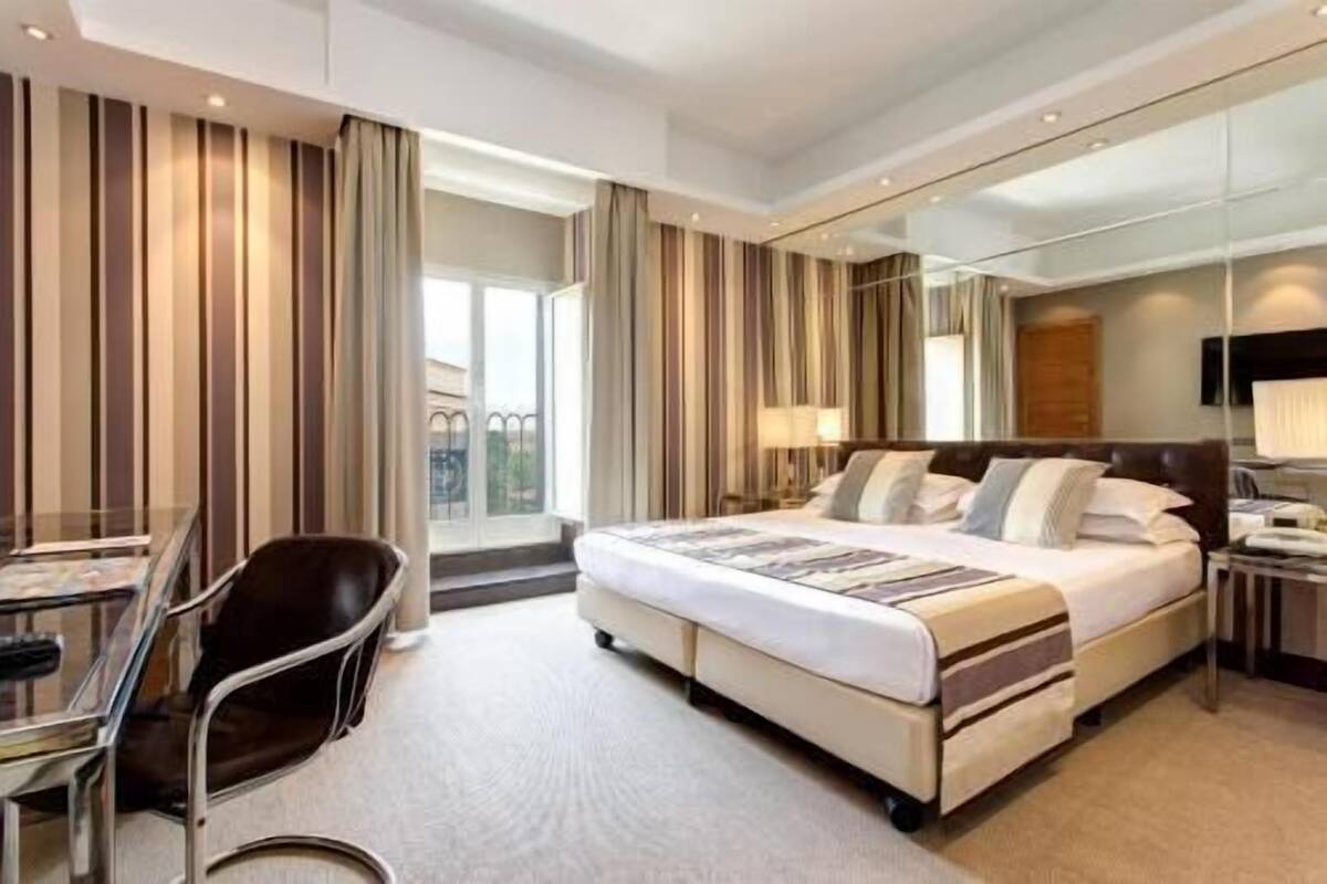 Una camera d'albergo con un letto, una scrivania, una sedia e un grande specchio.