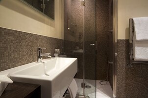 A modern bathroom with a large white sink, a glass-enclosed shower, and a towel hanging on the wall.