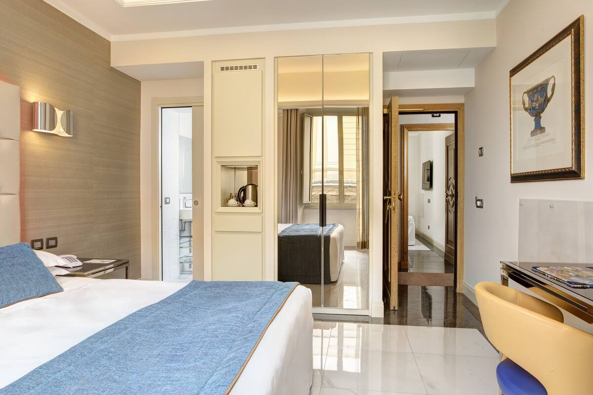 Una camera d'albergo con un letto, una scrivania, una sedia, uno specchio e una porta che dà su un bagno.