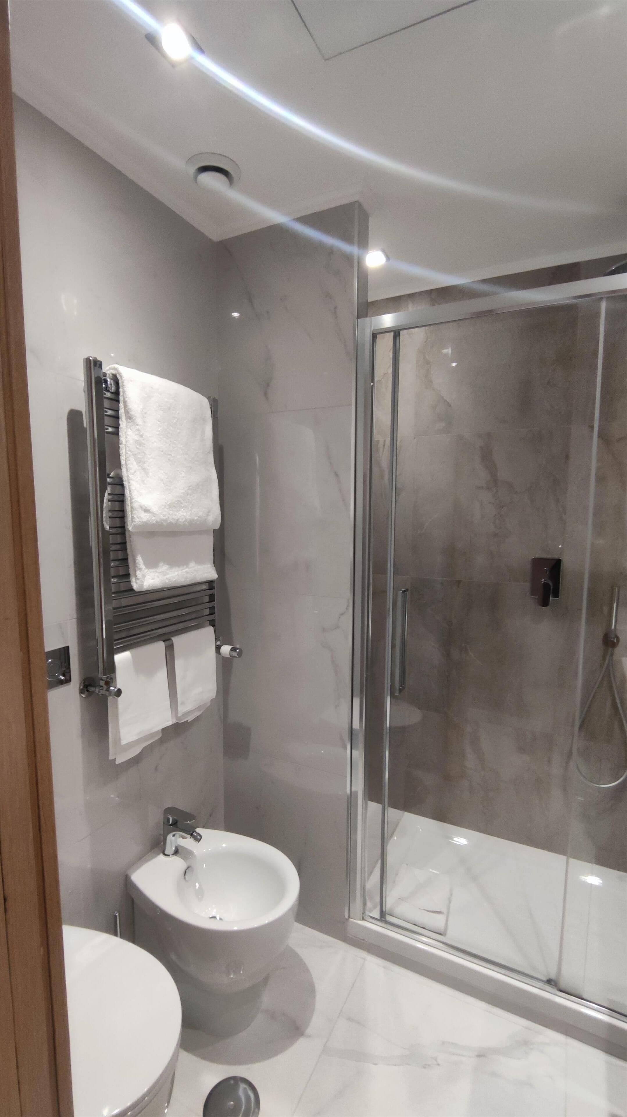 A modern bathroom with a glass-enclosed shower, a pedestal sink, and a towel rack with multiple towels.