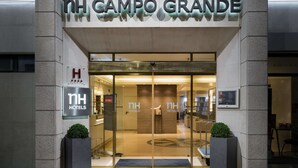 L’entrée de l’hôtel NH Campo Grande se distingue par sa façade moderne en verre, son espace d’accueil et un ascenseur bien visible.