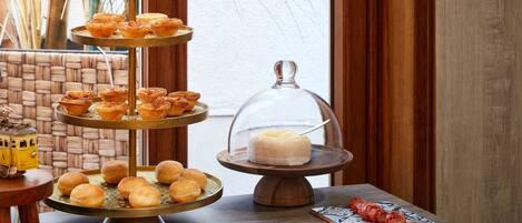Un présentoir à pâtisseries à trois niveaux, garni de diverses viennoiseries, un dessert présenté sous un cloche de verre et une assiette de charcuteries.