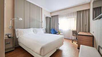 A hotel room with a large bed, a desk, a chair, and a lamp.