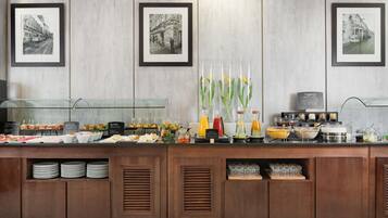 A buffet setup with various food items, framed pictures on the wall, and a coffee machine.