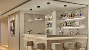 Un espace bar moderne avec un comptoir en bois, des tabourets de bar et des étagères remplies de bouteilles d’alcool.