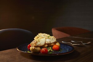 A plate of food with fish, potatoes, and cherry tomatoes on a dark plate.
