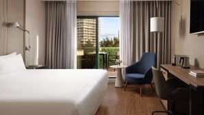 Une chambre d’hôtel avec un grand lit, un bureau avec une chaise, une télévision et un balcon avec des rideaux.