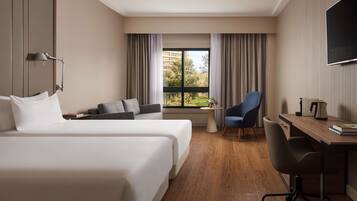 Habitación de hotel con dos camas, un escritorio, una silla, un televisor y una ventana con cortinas.
