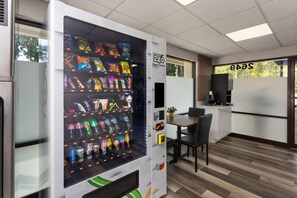 A vending machine stocked with snacks and drinks, a coffee machine, and a seating area with a table and chairs.