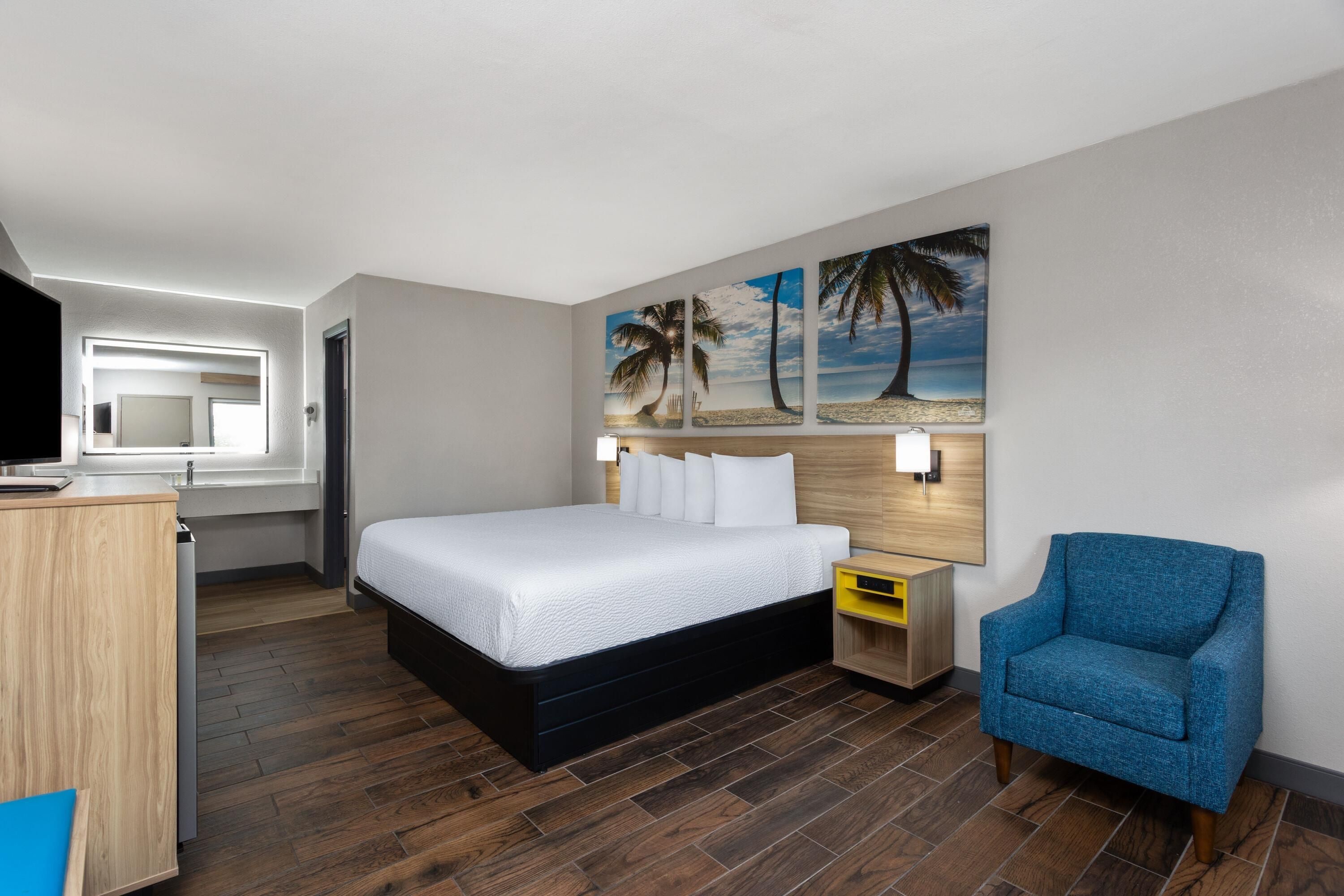 Una habitación de hotel con cama, escritorio, silla y un cuadro de una playa.