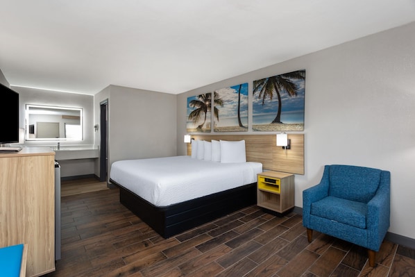 A hotel room with a bed, a desk, a chair, and a painting of a beach scene. - Days Inn by Wyndham Gainesville Hospital/University Area (Gainesville)