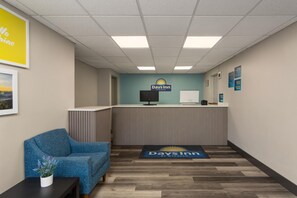 A reception area with a blue chair, a reception desk, a computer, and a logo for Days Inn. - Days Inn by Wyndham Gainesville Hospital/University Area (Gainesville)