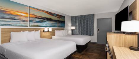 A hotel room with two beds, a TV, a desk, and a painting of a sunset over the ocean.