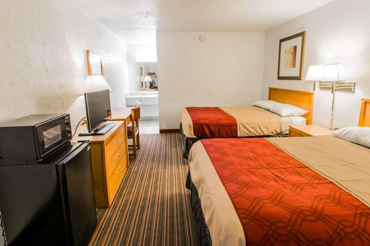Habitación de hotel con dos camas, un escritorio con televisor, microondas y un baño a la vista.