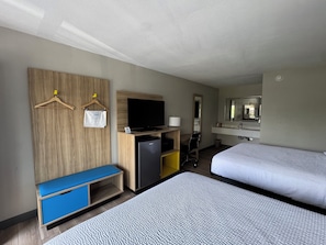 A hotel room with two beds, a TV, a desk with a computer, a mirror, and a small seating area.