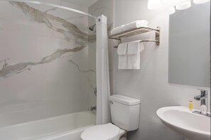 A bathroom with a marble wall, a shower, a toilet, a sink, and a towel rack. - Days Inn by Wyndham Gainesville Hospital/University Area (Gainesville)