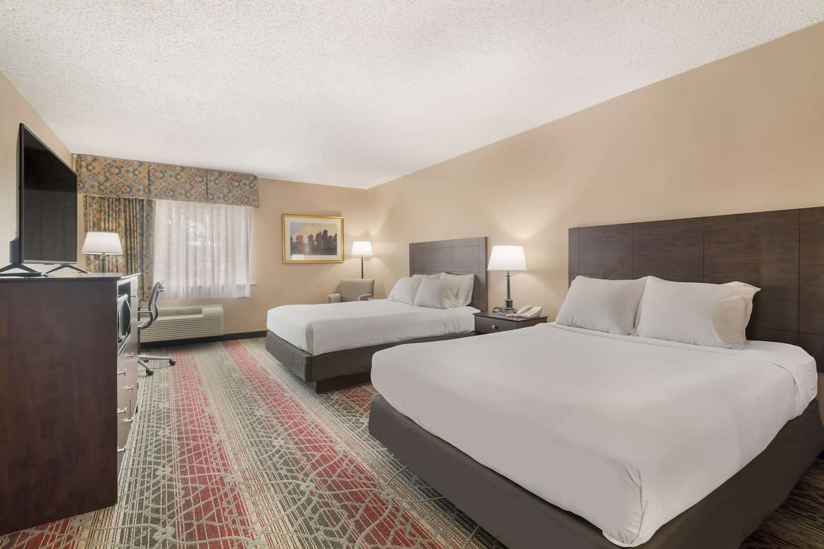 A hotel room with two beds, a desk, a chair, a TV, and a painting on the wall.