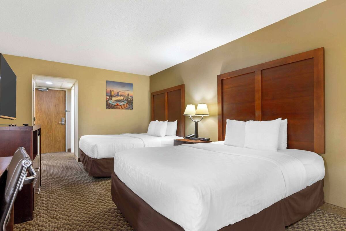A hotel room with two beds, a desk, a chair, a lamp, and a painting on the wall.