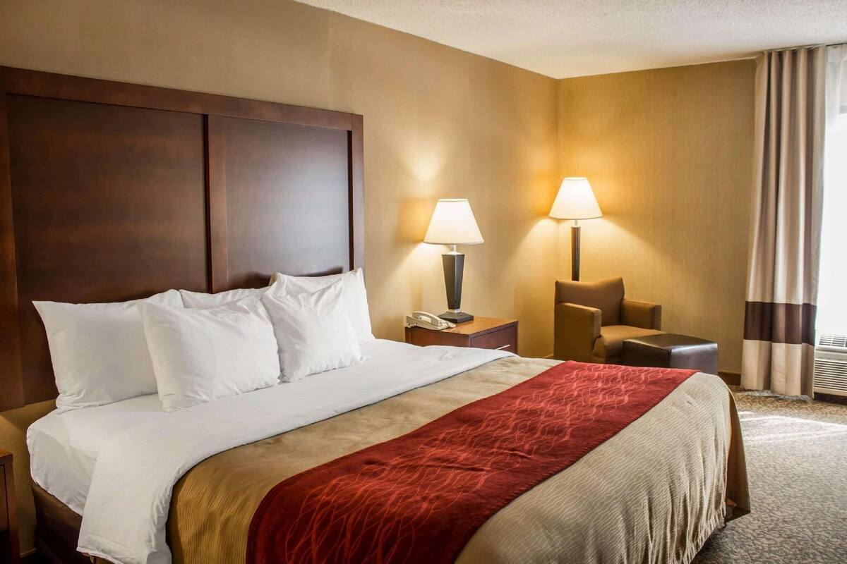A hotel room with a large bed, two bedside tables, a chair, and a window with curtains.