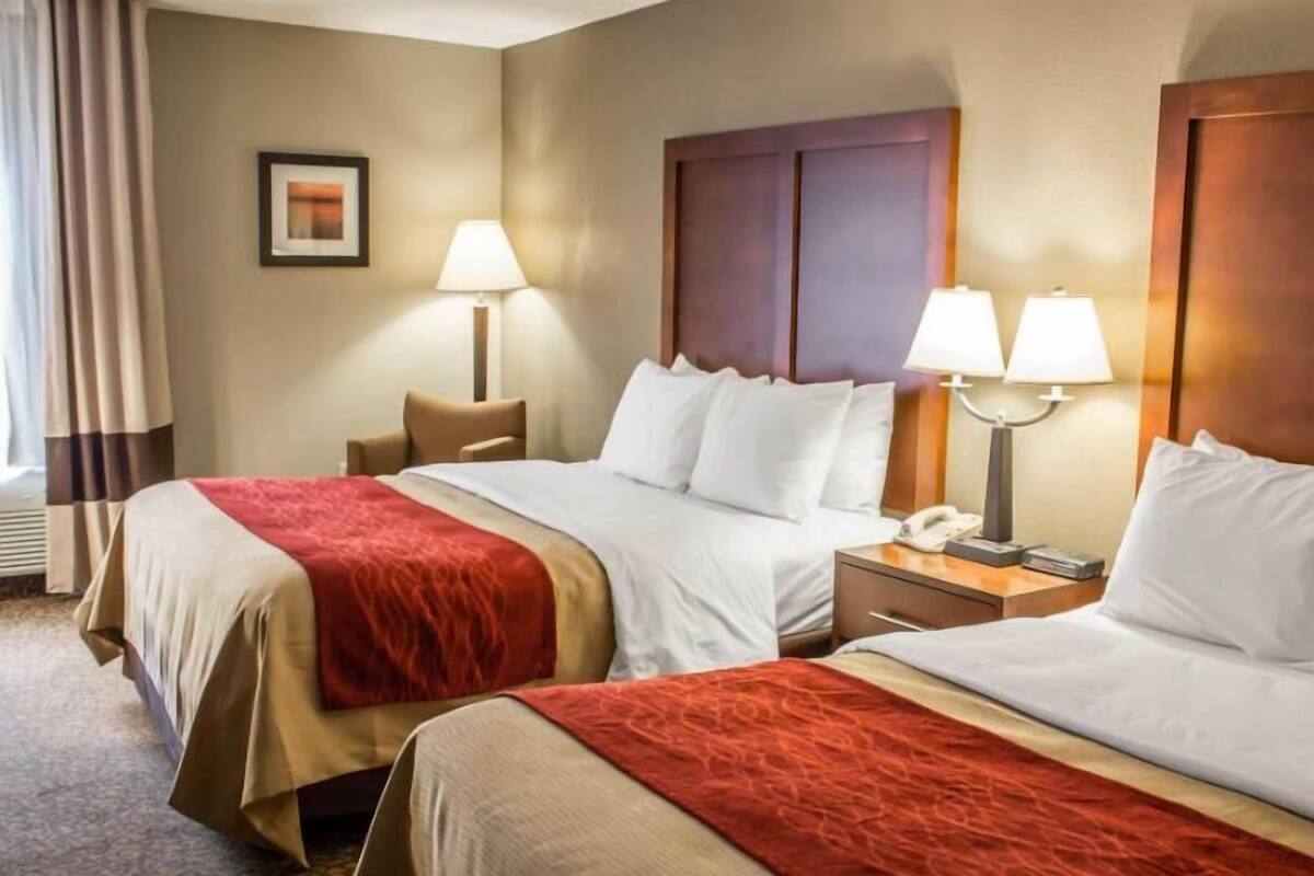 A hotel room with two beds, a nightstand with a phone, and a lamp.