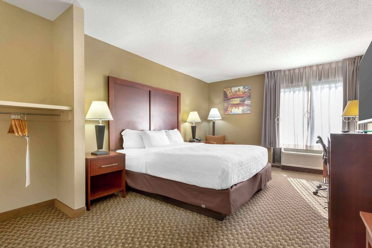 A hotel room with a large bed, two bedside tables with lamps, a desk, and a chair.