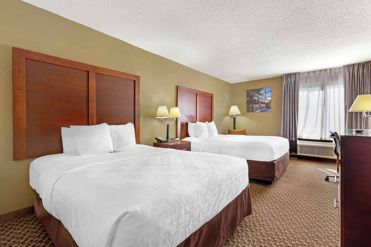 A hotel room with two beds, a desk, and a large window with curtains.
