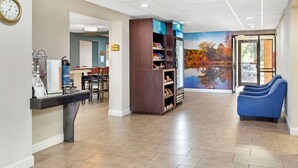 A reception area with a coffee station, a clock, a reception desk, a bookshelf, and a mural of autumn trees. - Clarion Pointe Durham Research Triangle Park (Durham)