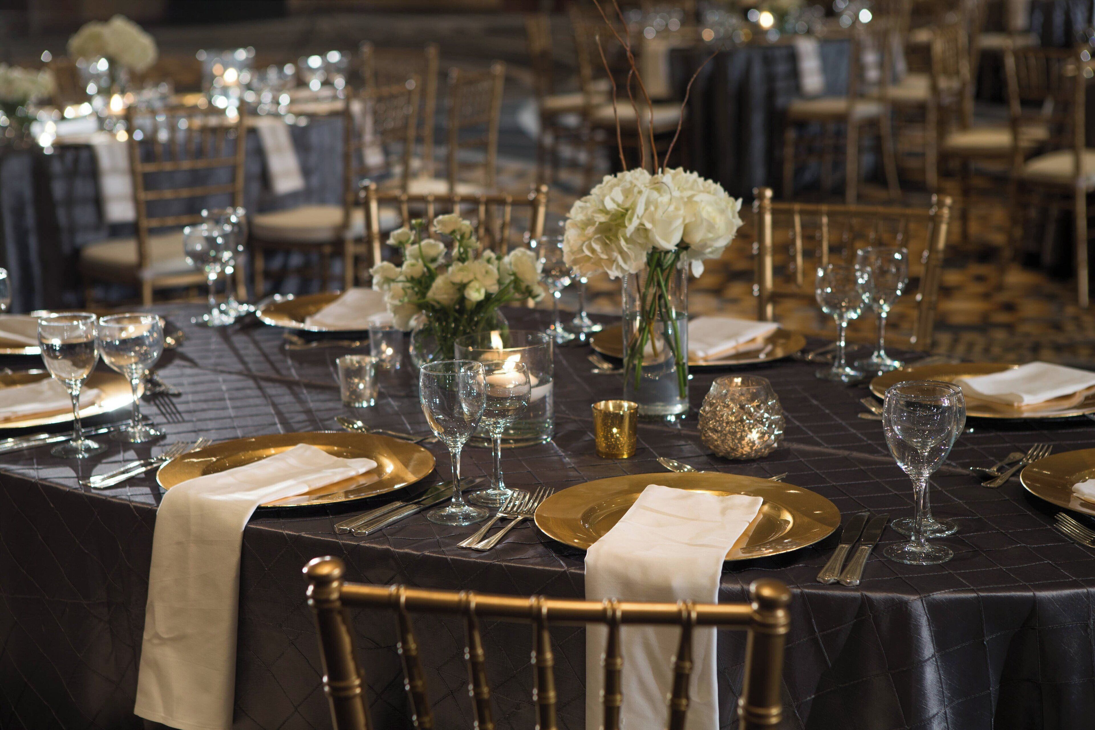 A banquet table set with gold and white tableware, white flowers, and candles.