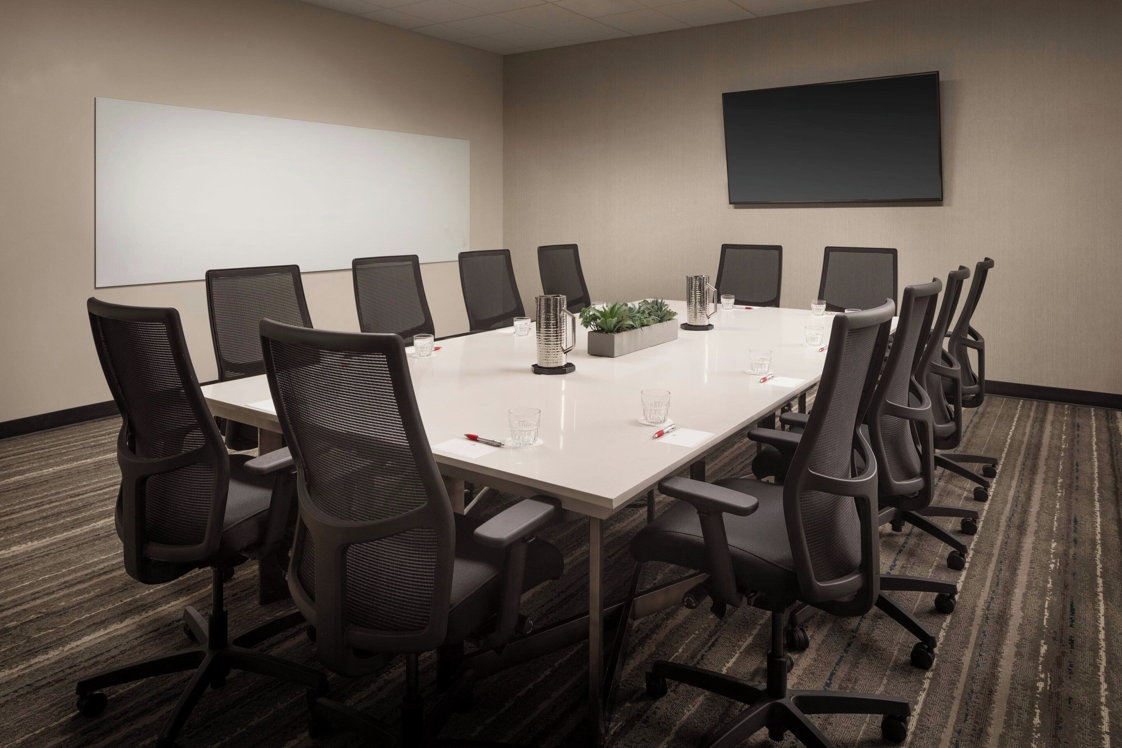 A conference room with a long table, black chairs, a projector screen, and a carpeted floor.